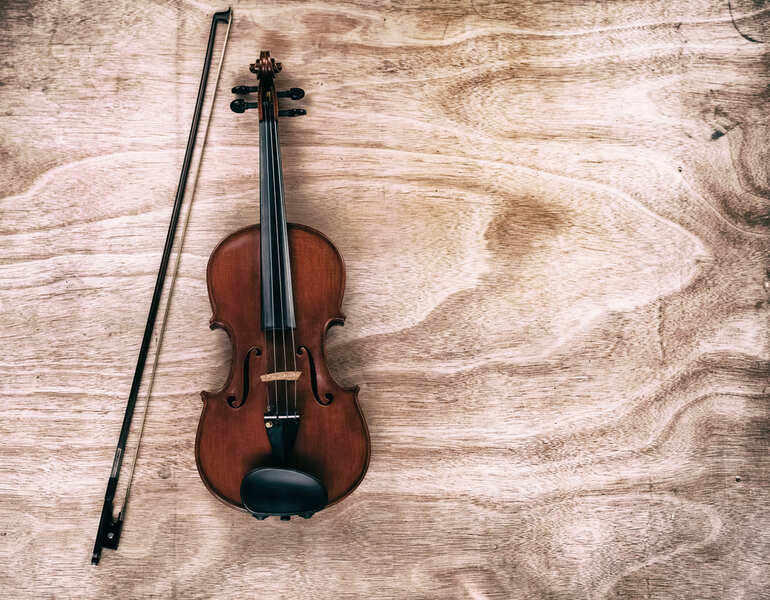 A cheap violin and bow on a wooden board with an abstract art background