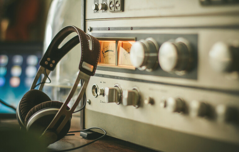 Vintage headphones resting on a wooden table with a retro college radio in the background