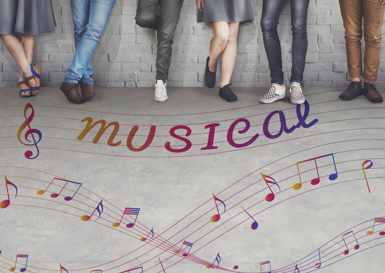 A group of university students gathered near a colorful wall, smiling and holding scripts, evoking the vibrant energy of musical theater
