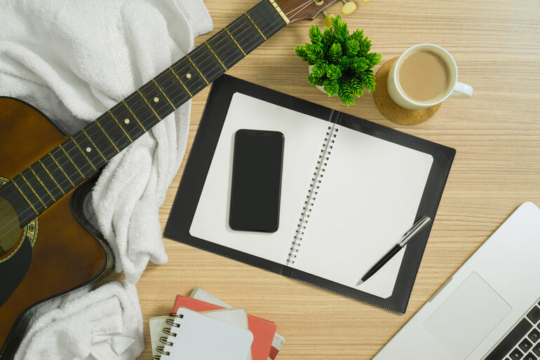 Study desk with guitar, notebook, coffee, and laptop