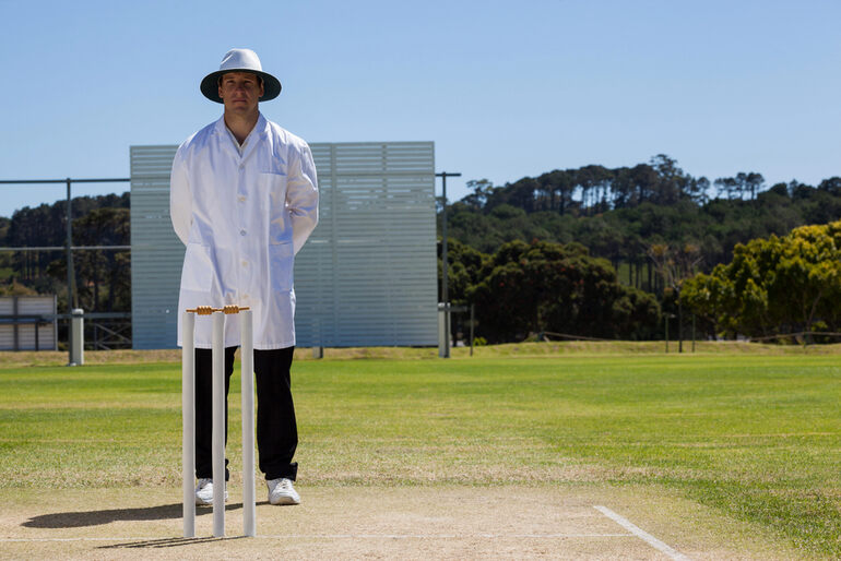 A cricket umpire standing on the pitch in full uniform.