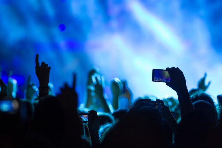 Live music concert crowd with hands raised and phones recording under vibrant blue stage lighting