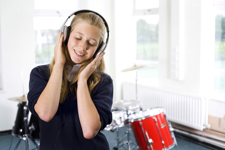 Smiling student enjoying music on headphones in a classroom with drums in the background