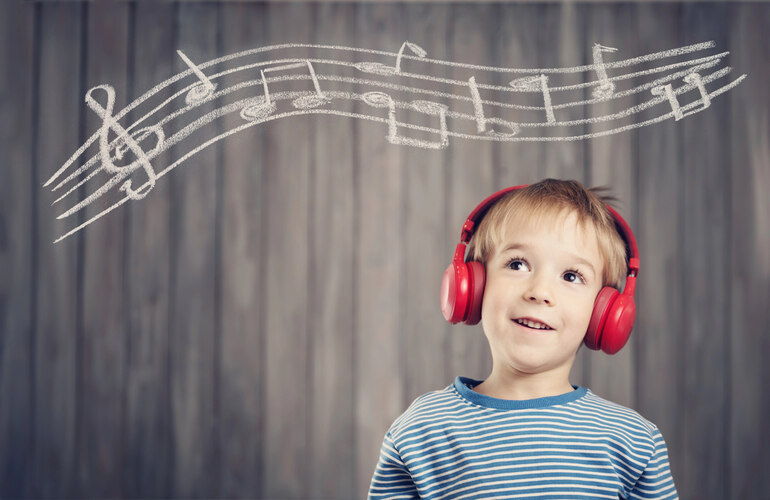 Smiling child wearing red headphones, looking up at chalk-drawn musical notes, symbolizing the impact of in-home music lessons on children's creativity and growth