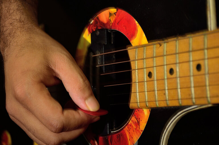 Close-up of a beginner guitarist strumming an acoustic guitar with a colorful soundhole design