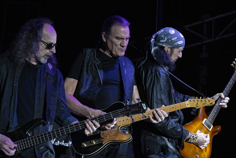Three energetic rock musicians performing under bright stage lights