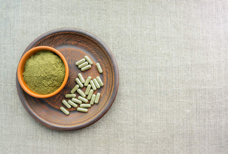 Green Maeng Da kratom on a wooden plate over a linen background