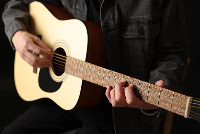 Beginner practicing acoustic guitar, focusing on finger placement and technique