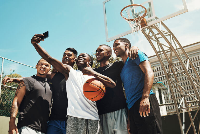 Group of young men smiling and taking a selfie on an outdoor basketball court