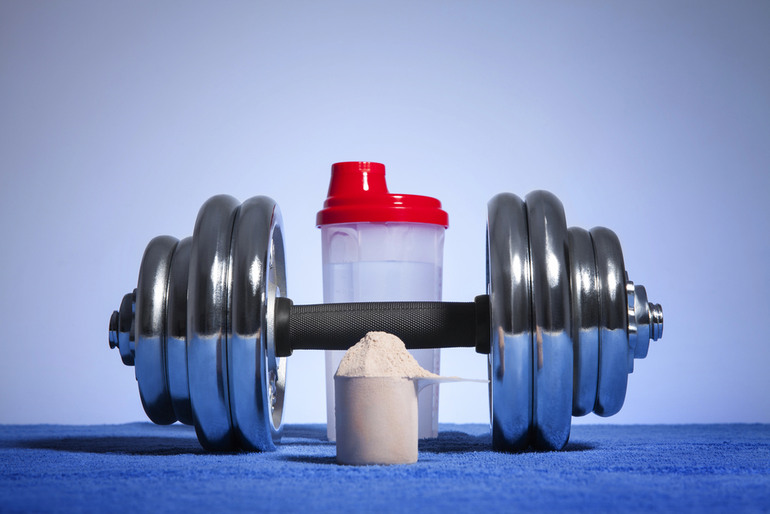 Dumbbell, protein powder scoop, and shaker bottle placed on a blue surface