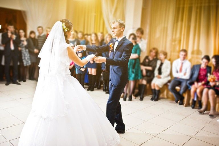 Bride and groom sharing their first dance at a wedding reception, surrounded by guests.