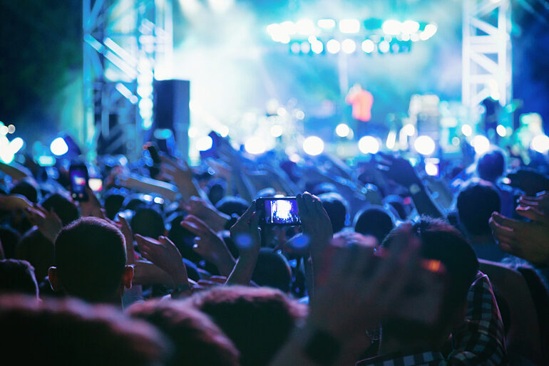 Fans recording and enjoying a live music concert with bright stage lights.