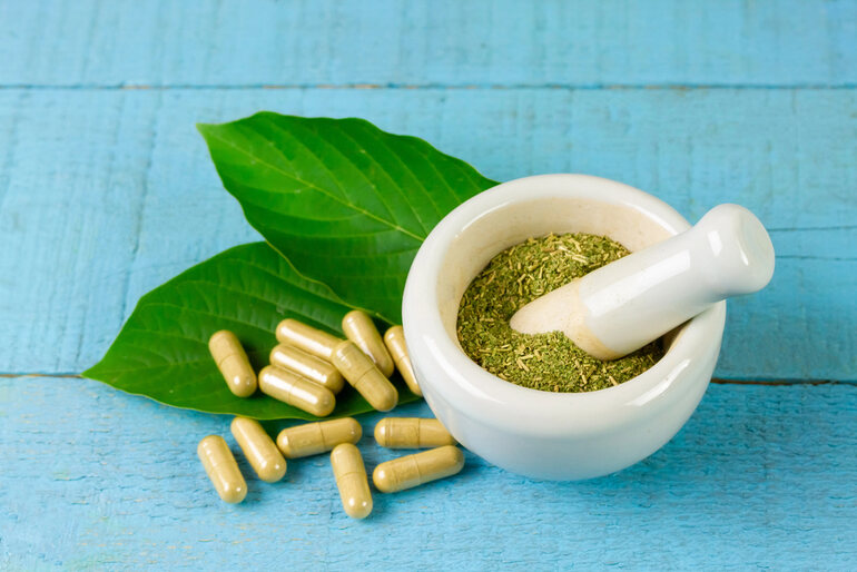 Kratom capsules and powdered leaves in a mortar with a pestle for safe buying and delivery.