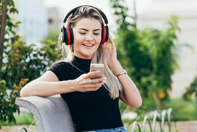 Woman enjoying music on headphones while using a dating app outdoors