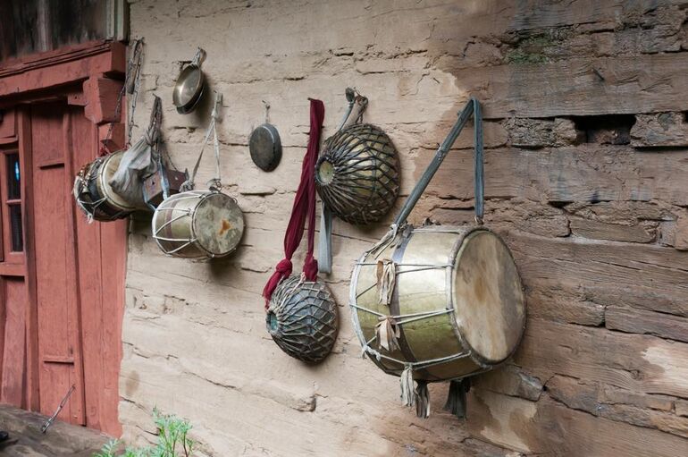Traditional handmade drums and folk percussion instruments hanging on a rustic mud wall in a rural village.