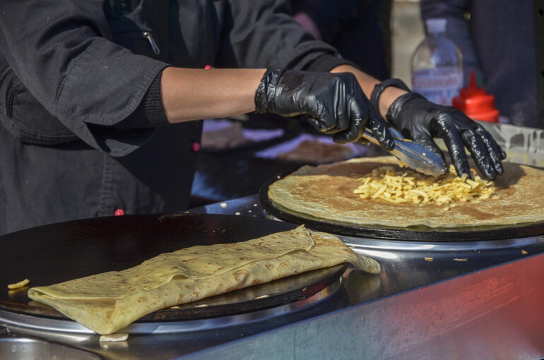 A street food vendor preparing cheesy crepes on a hot griddle at a music festival