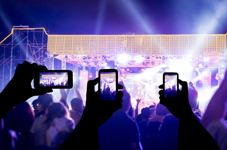 Fans capturing a live music concert with smartphones, colorful stage lights, and crowd energy