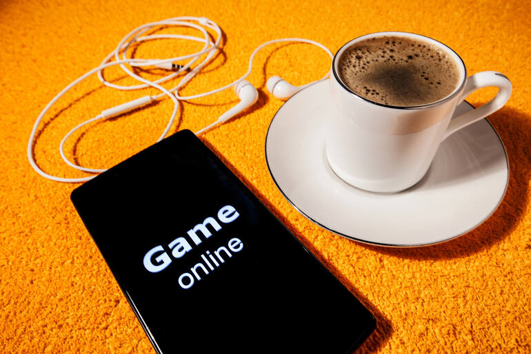 Smartphone displaying "Game online" next to a cup of coffee and earphones on a vibrant orange background
