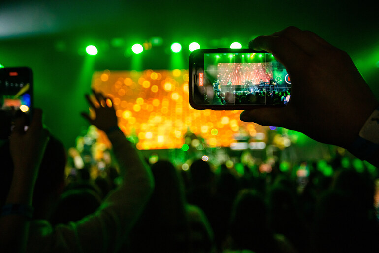Fans recording a live concert with smartphones under green lights.