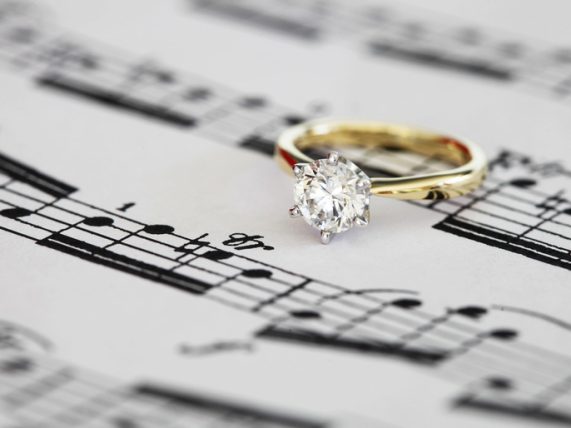 Gold diamond engagement ring resting on a sheet of romantic music notes, symbolizing the harmony of love and proposals.
