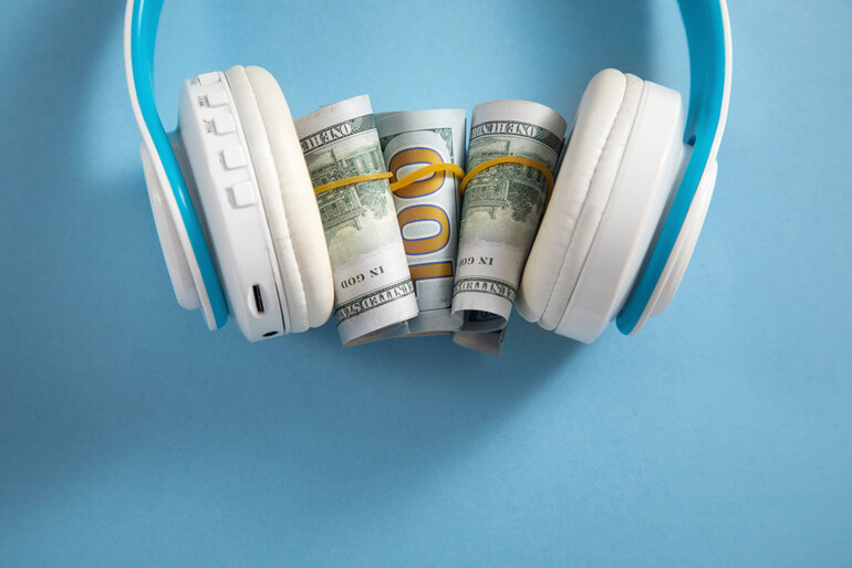 Rolled dollar bills inside headphones symbolizing fast payouts and music-themed earnings.