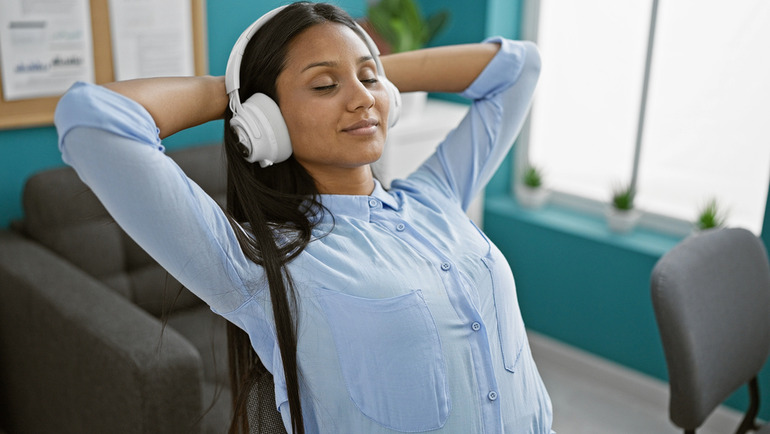 A relaxed woman wearing headphones sits back in her chair, enjoying music in a calm office setting, symbolizing harmony and hormone balance.