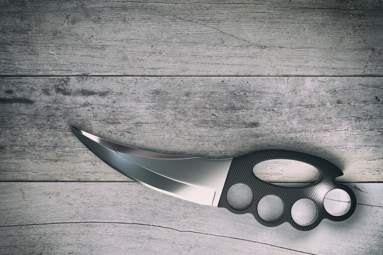 A sleek karambit knife with a curved blade and knuckle grip handle resting on a wooden surface.