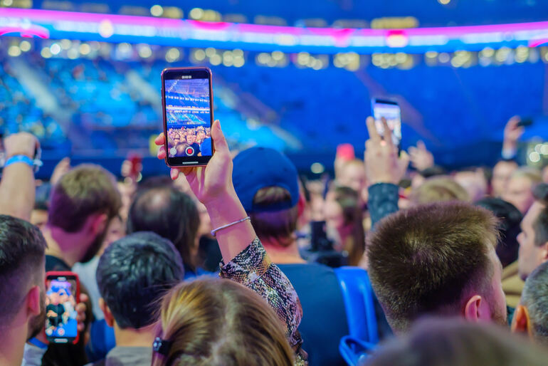 Crowd of fans at a live concert holding up smartphones to record and livestream the event
