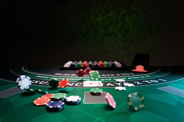 Poker chips and playing cards scattered on a casino blackjack table under dim lighting, with music in the casino.