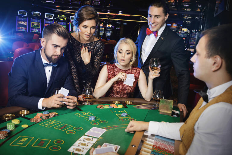 Group of elegantly dressed people playing cards, enjoying drinks and music at a casino, representing the excitement of real money gambling.