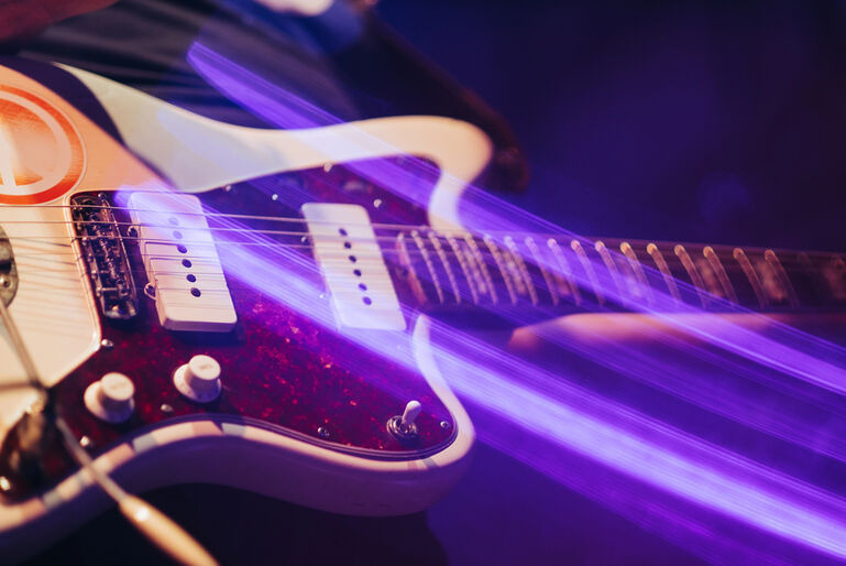 Electric guitar under vibrant stage lights representing the evolution of live music performances from instruments to holograms