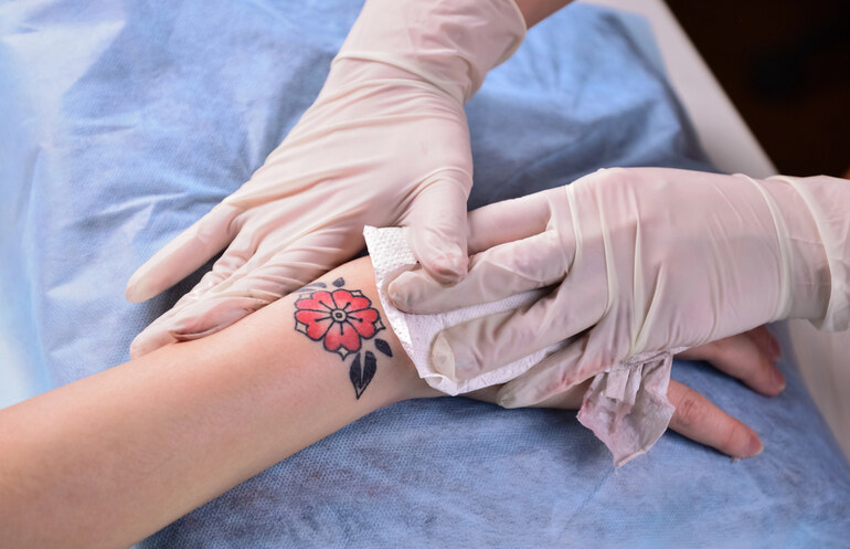 A professional wearing medical gloves gently cleaning a small flower tattoo on a person’s wrist