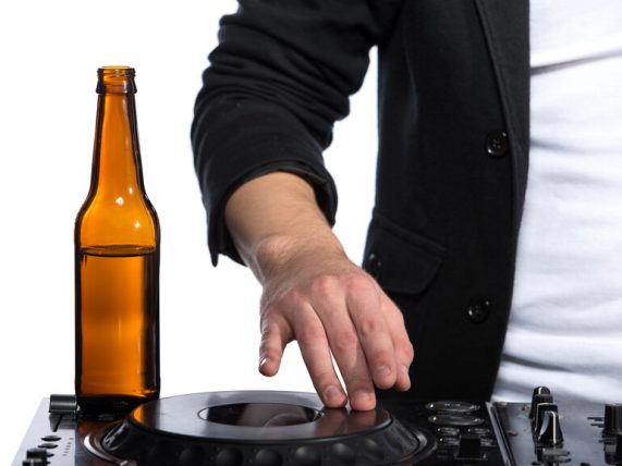 A disc jockey is playing music while having a bottle of beer