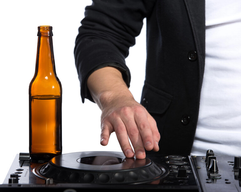 A disc jockey is playing music while having a bottle of beer