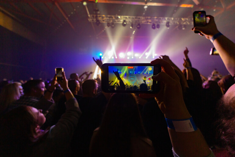 Digital platform technologies are enhancing modern live music experiences through smartphone recording at a concert.