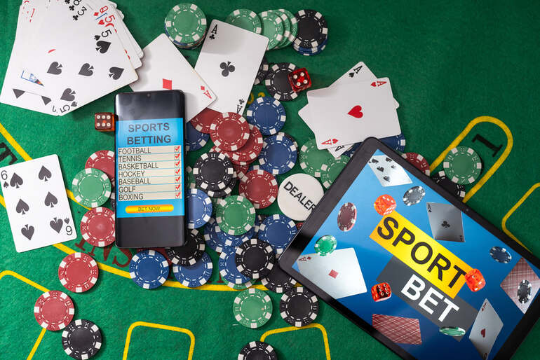 Smartphone and tablet displaying sports micro-betting apps surrounded by poker chips and playing cards on a casino table.