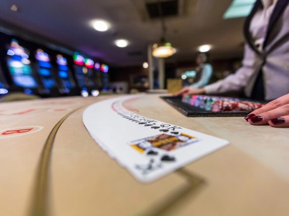 A casino dealer’s hand beside a spread of playing cards on a gaming table