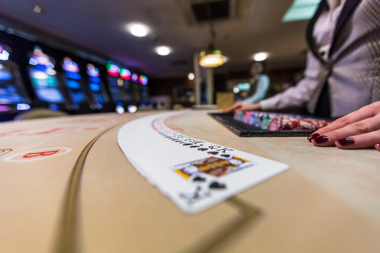 A casino dealer’s hand beside a spread of playing cards on a gaming table