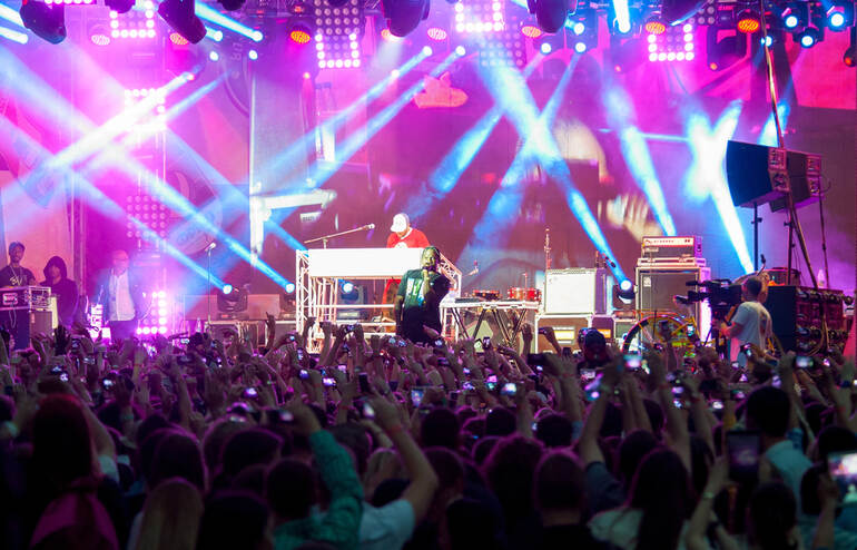 Crowd enjoying a vibrant live performance on a brightly lit stage at a major European music festival.