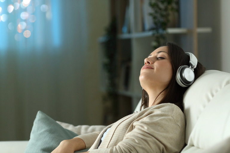 A woman relaxing on a couch with headphones, listening to music to unwind after a long day.