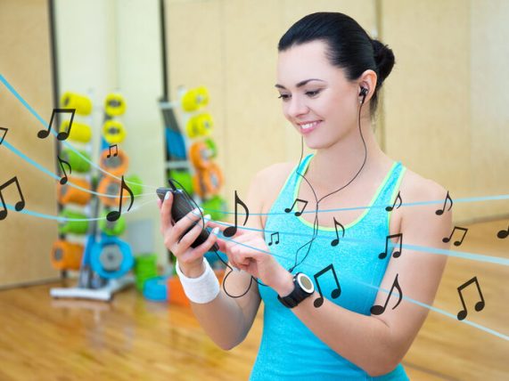 Smiling cheerful athlete in a gym listening to premade cheer music mixes on her phone to power through practice and refine her routine.
