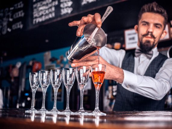 Event bartender pouring cocktails into glasses behind the bar