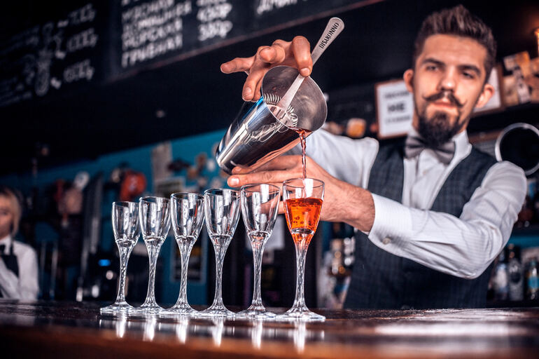 Event bartender pouring cocktails into glasses behind the bar