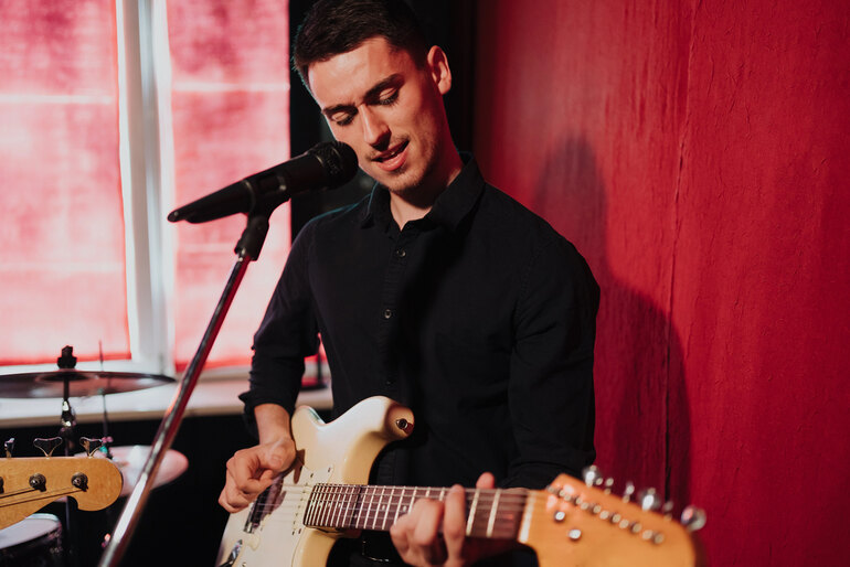 Singer is a beginner who rehearses his vocals in the home studio by playing the guitar