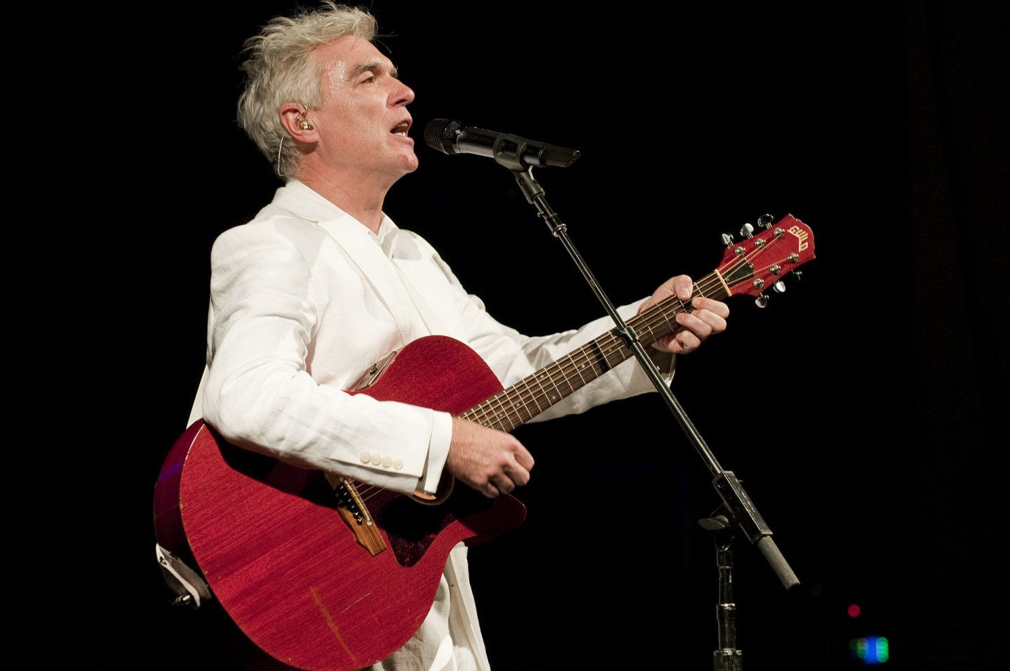 David Byrne singing with a red guitar and white suit.