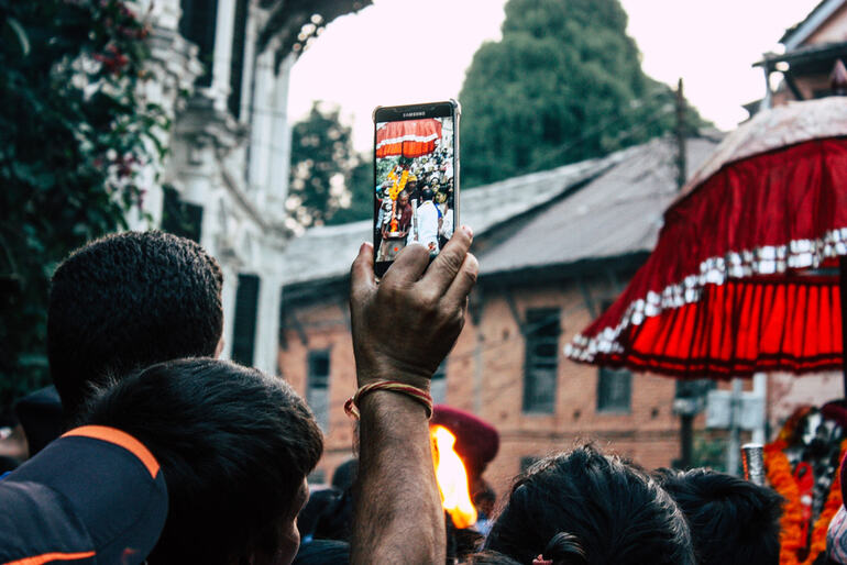 Person in a crowd holding up a smartphone to record a street festival procession.