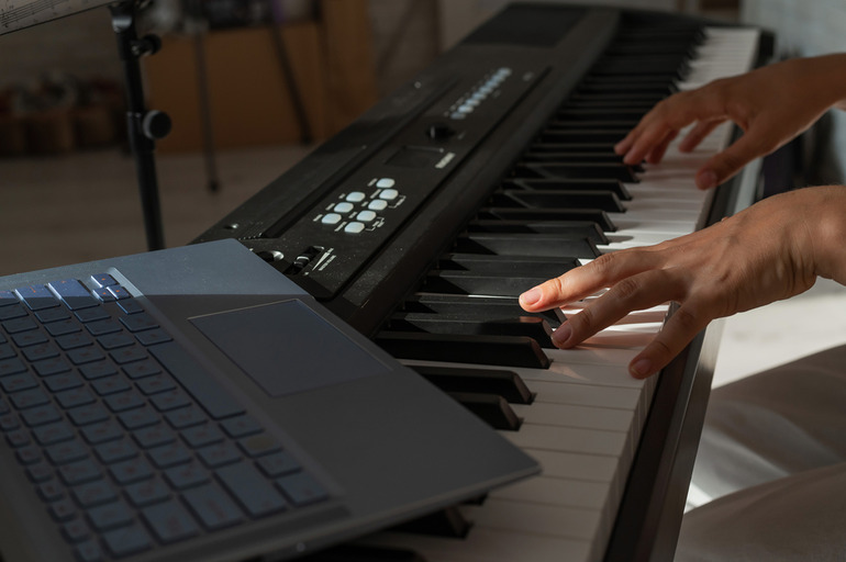 Musician playing a premium digital piano with a laptop nearby, highlighting acoustic and digital piano options for all skill levels.
