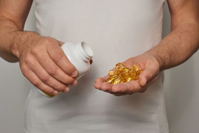 Man in a white shirt pouring yellow supplement capsules from a bottle into his hand