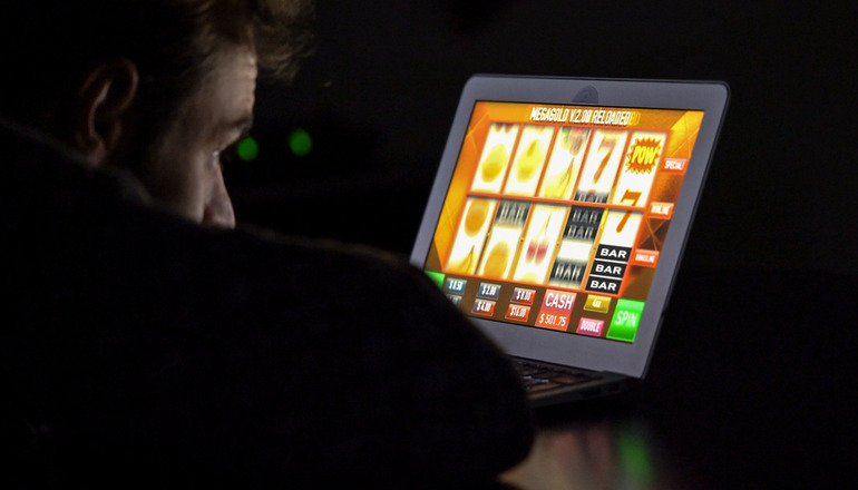 A man in front of an online casino slot machine on a laptop