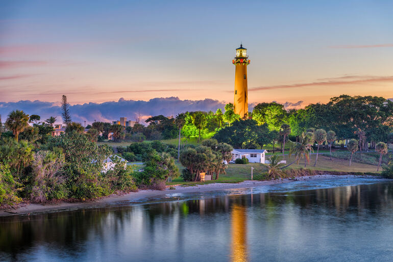 Scenic sunset view of a coastal lighthouse in South Carolina, surrounded by lush greenery and calm water